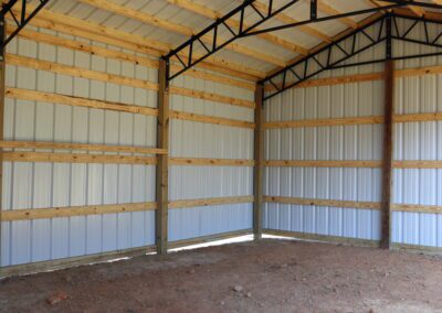 Interior of an empty metal barn with wooden beams and a dirt floor.