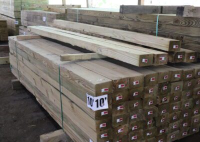 Stacks of treated lumber in a warehouse with labels indicating sizes.