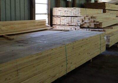Stacks of treated lumber in a warehouse with labels indicating sizes.