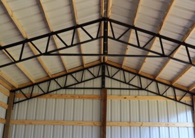 Interior of an empty metal barn with wooden framing and dirt floor.